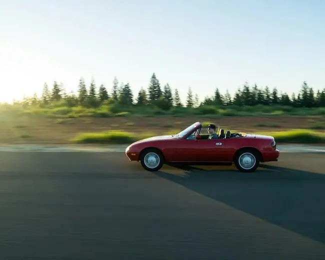 Un cabriolet rouge décapoté roule rapidement dans la campagne